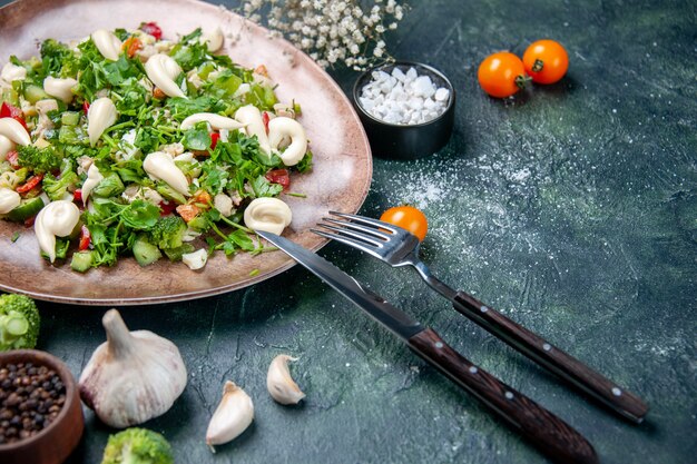 front view vegetable salad inside elegant plate with cutlery on a dark blue background