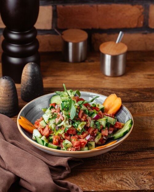 Овощной салат с лимоном на тарелке на коричневом деревянном столе, овощной салат, вид спереди