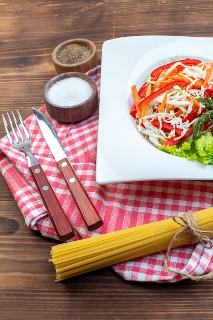 茶色の表面に調味料とパスタを添えた正面図の野菜サラダ