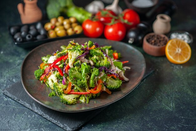 Front view of vegetable salad with various ingredients and fork on black cutting board on dark background