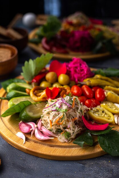 Вид спереди нарезанные овощи и салат из целых огурцов на коричневом деревянном столе вместе с буханками хлеба на сером столе с витаминными растениями