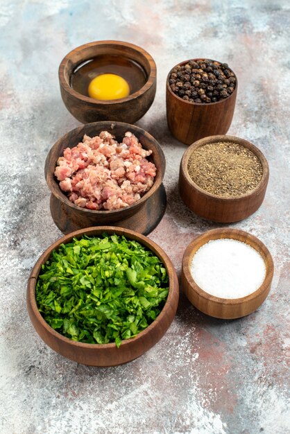 Вид спереди вертикальные рядные миски с мясной зеленью, яичный желток, перец, порошок, черный перец, соль, на обнаженном фоне