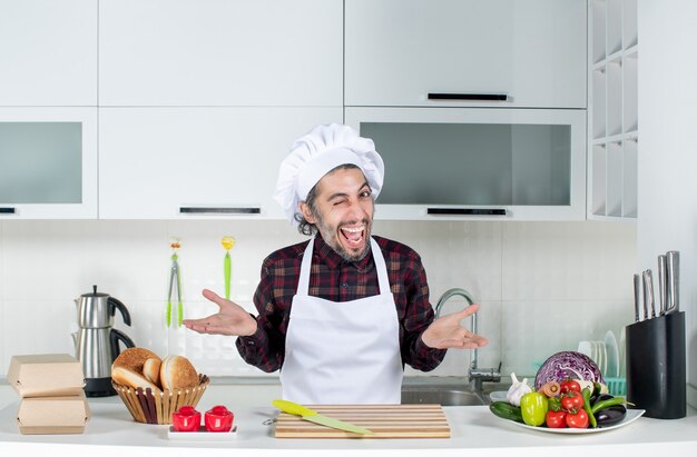 Front view of very excited man blinking eye standing behind kitchen table in the kitchen