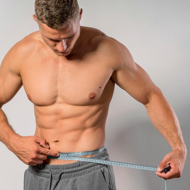 Front view of very fit man holding measuring tape around waist