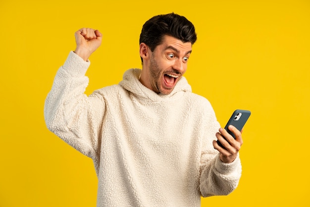 Front view of victorious man holding smartphone