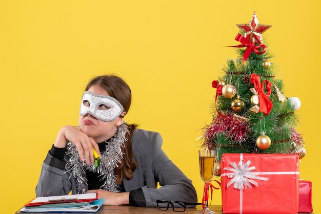 Foto gratuita vista frontale vagava giovane ragazza con la maschera di travestimento seduto al tavolo albero di natale e regali cocktail