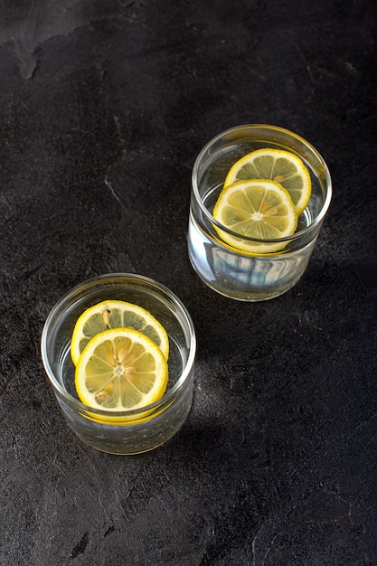 Un'acqua vista frontale con bevanda al limone con limoni a fette all'interno di bicchieri trasparenti sul buio