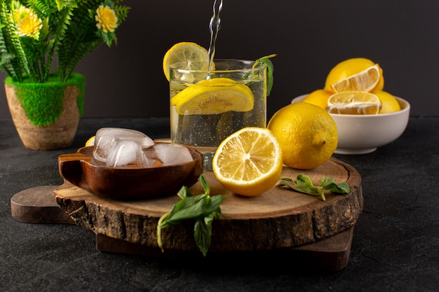 녹색에 쏟아지는 유리 안에 레몬 신선한 시원한 음료와 함께 전면보기 물 어둠에 얇게 썬 레몬 아이스 큐브와 나뭇잎