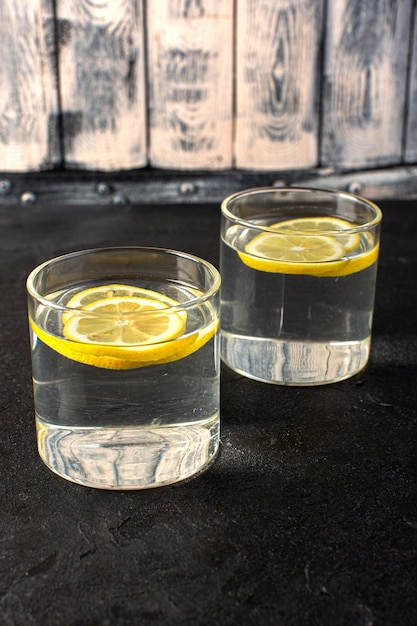 Una vista frontale acqua con limone fresca bevanda fresca con fette di limoni all'interno di vetri trasparenti sul buio