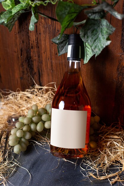Бутылка виски, вид спереди, зеленый виноград и зеленые листья, изолированные на коричневом фоне.