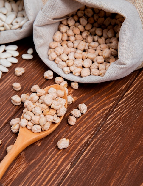 Front view white beans with peas in a burlap bag with wooden spoons on a wooden surface