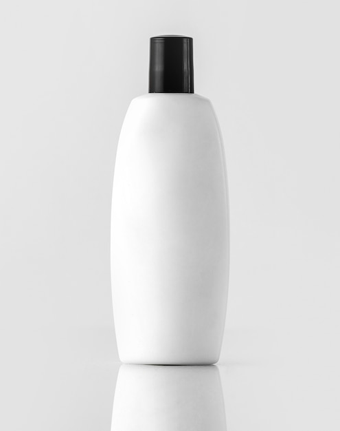 Белый шампунь в бутылках с черным колпачком, изолированный на белой стене