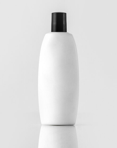 Белый шампунь в бутылках с черным колпачком, изолированный на белой стене
