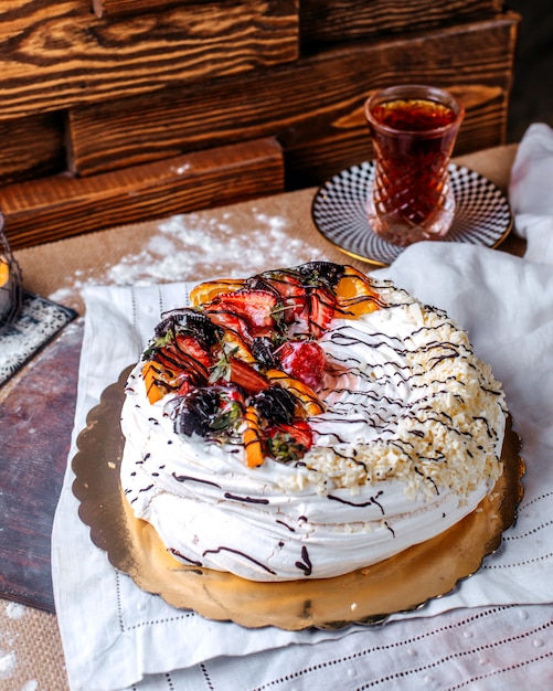 Front view white cake tasty sweet along with fresh sliced fruits on top and hot tea on the brown desk