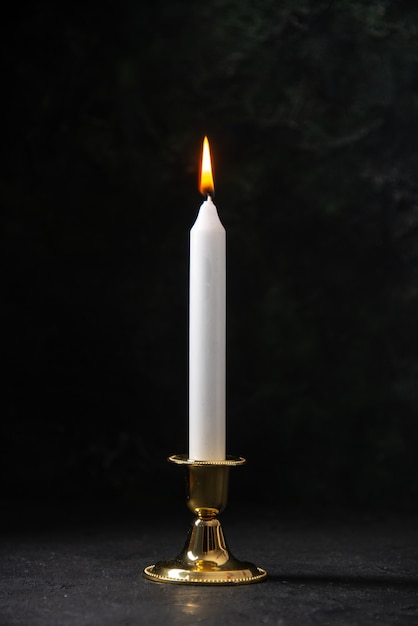 Front view of white candle in golden stand on black