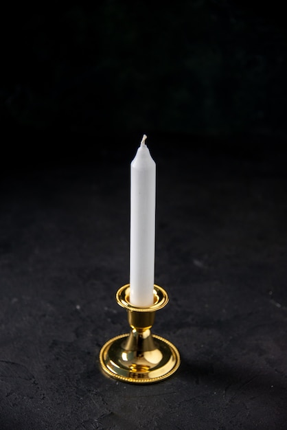 Вид спереди белой свечи в золотой подставке на черном