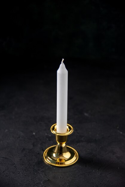 front view of white candle in golden stand on black