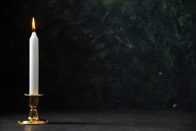 Вид спереди белой свечи в золотой подставке на черном