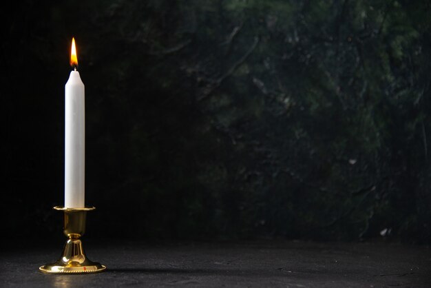 Front view of white candle in golden stand on black