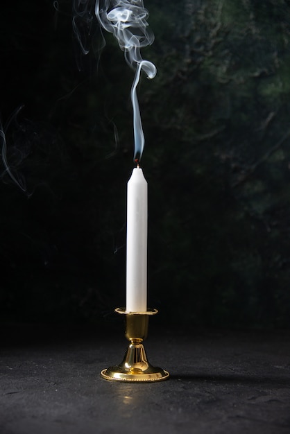 Front view of white candle in golden stand on black