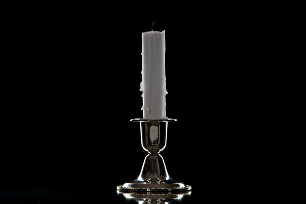 Front view of white candle in golden stand on black