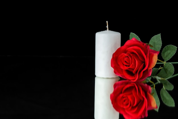 Front view of white candle with red rose on black