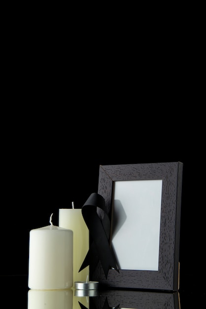 Front view of white candles with picture frame on black wall