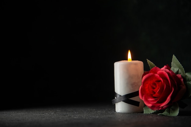 Front view of white candles with red flower on dark wall