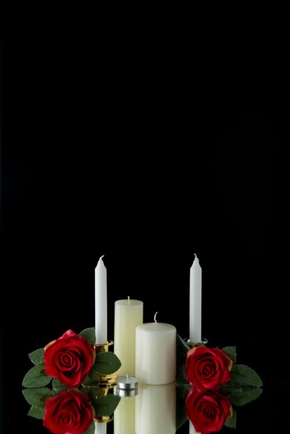 Front view of white candles with red flowers on black wall