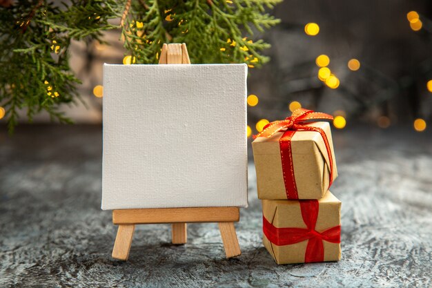어두운 배경에 나무 이젤 선물 상자 크리스마스 조명에 전면 보기 흰색 캔버스