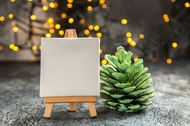 Front view white canvas on wood easel xmas lights green pinecone on dark