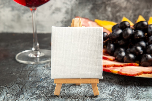 Foto gratuita tela bianca vista frontale su cavalletto in legno fette di carne di uva vino su piatto di legno su oscurità