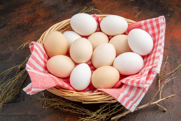 Вид спереди белые куриные яйца внутри корзины с полотенцем на темной поверхности