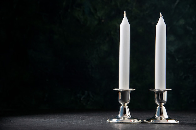 Front view of white long candles on a dark wall