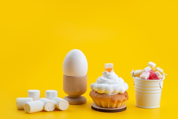 Вид спереди белый зефир вместе с тортом и конфетами на желтом столе, сахарная конфета сладкого бисквитного цвета