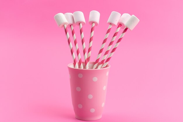 A front view white marshmallows with pink sticks inside pink cup on pink