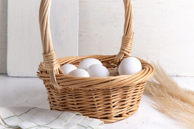 Front view white whole eggs inside basket on white desk.
