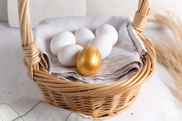 Вид спереди белые целые яйца внутри корзины с золотым на белом столе.