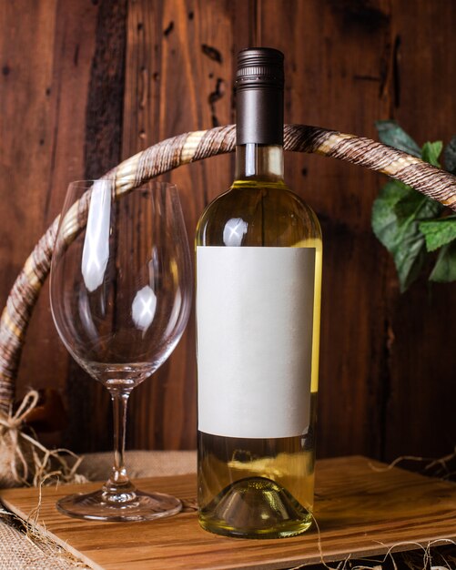 Фронтальная бутылка белого вина вместе с пустым стаканом на деревянном столе