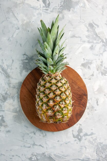 Front view of whole fresh golden pineapple on cutting board on marble surface