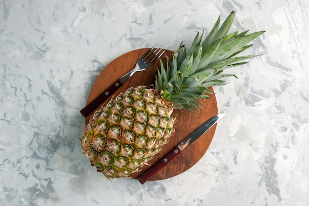 Front view of whole fresh golden pineapple on cutting board with fork and knife on marble surface