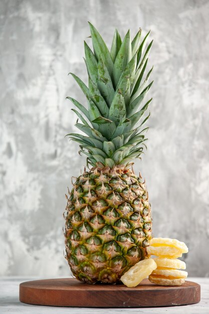 Front view of whole fresh golden pineapple and limes on cutting board standing on marble surface