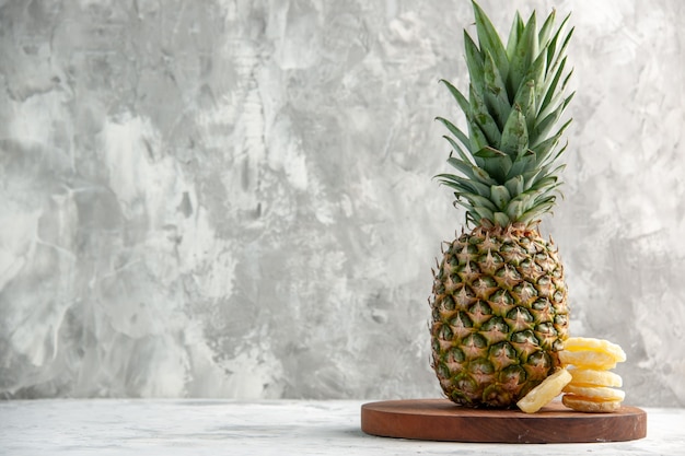 Front view of whole fresh golden pineapple and limes on cutting board standing on marble surface