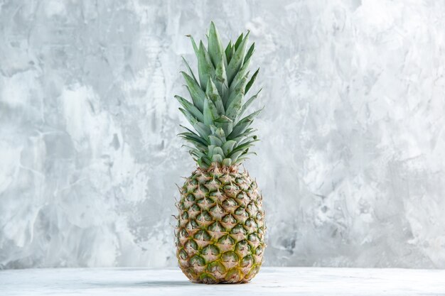 Front view of whole fresh golden pineapple standing on marble surface