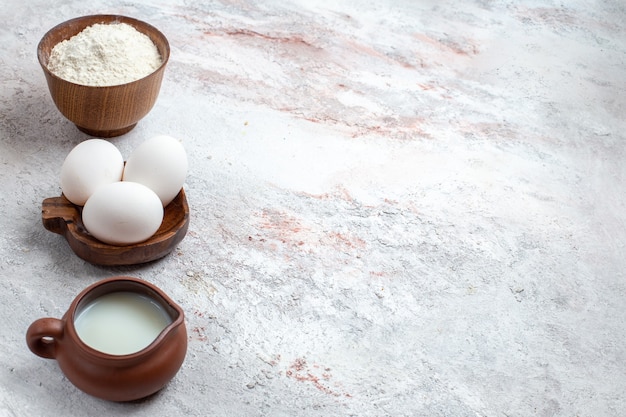 Вид спереди цельные сырые яйца с мукой и молоком на светлом белом фоне яичный сырой завтрак еда еда