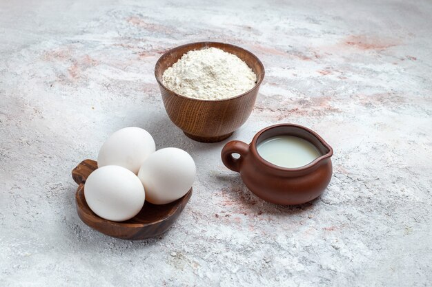 Front view whole raw eggs with flour and milk on white surface egg raw breakfast meal food