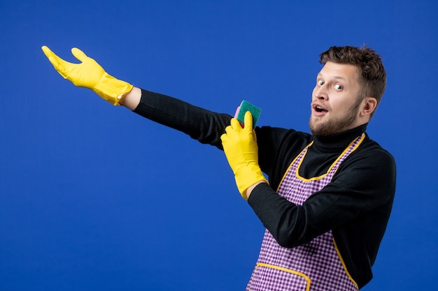 Free photo front view of wide-eyed male housekeeper holding sponge standing on blue wall