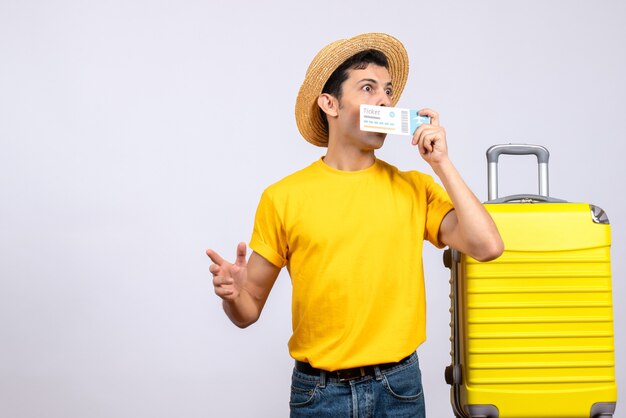 Free photo front view wide-eyed young tourist standing near yellow suitcase holding ticket