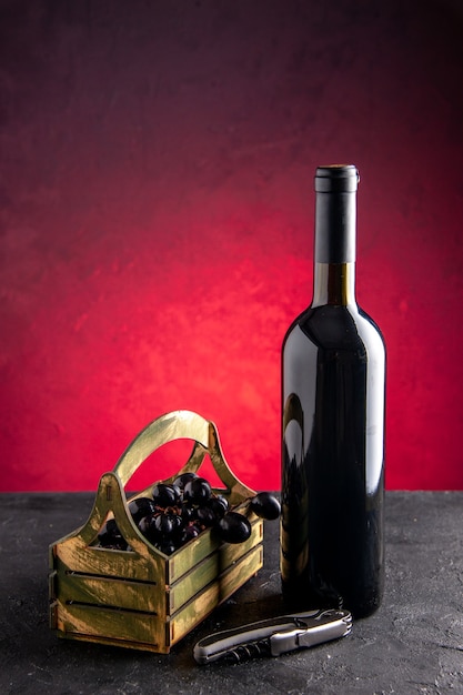 Vista frontale bottiglia di vino uva nera in scatola di legno apribottiglie su sfondo rosso chiaro