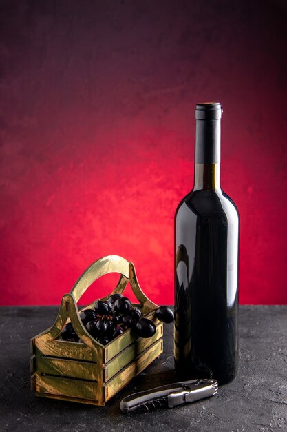 明るい赤の背景に木製の箱のワインオープナーで正面図のワインボトル黒ブドウ